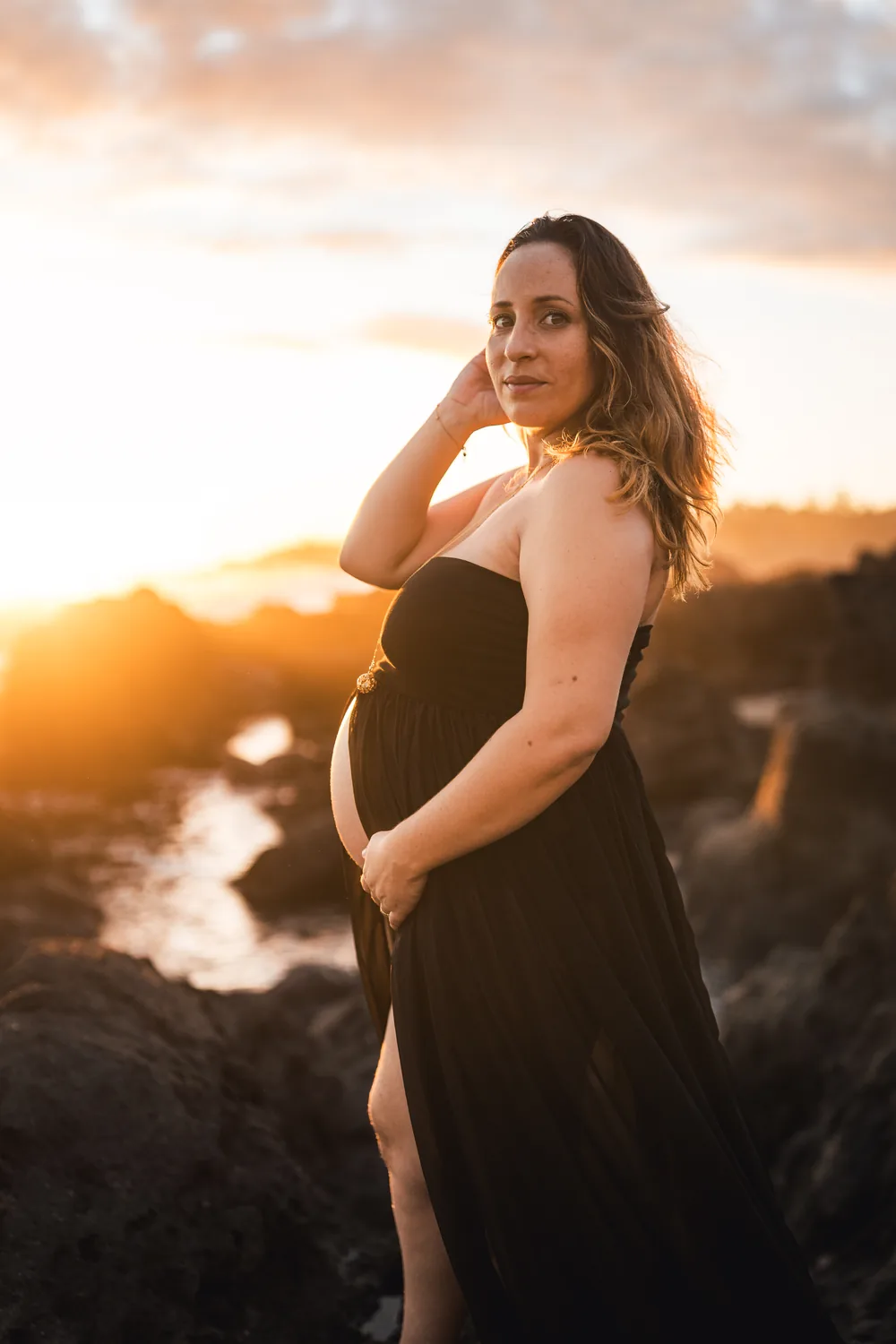 Future maman en robe noire à contre-jour sur la plage