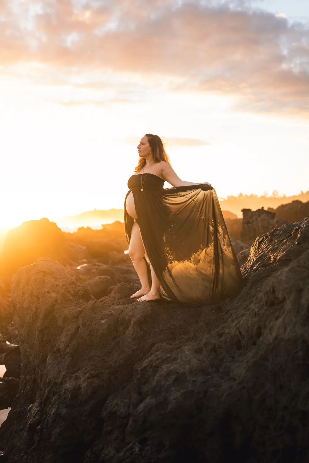 Silhouette de future maman sur un rocher face au soleil couchant